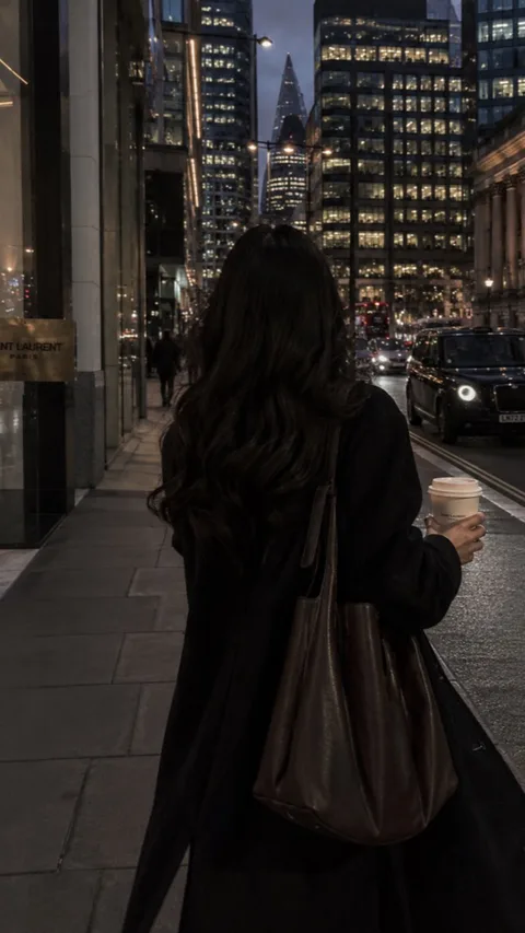 A person walking through the city with a coffee at dusk.